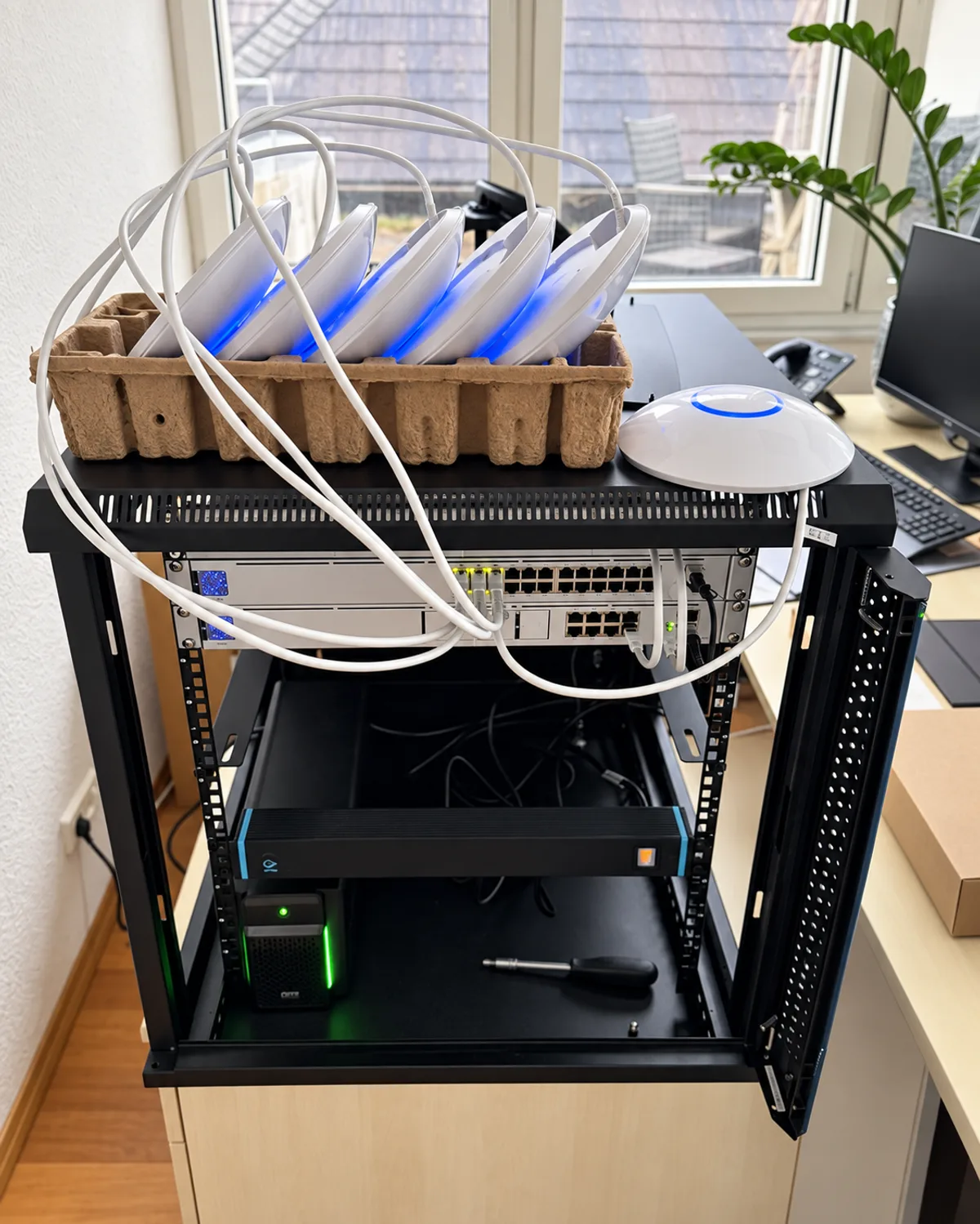 Sechs Access Points liegen angeschlossen in einer Verpackungsschale auf dem offenen Netzwerkschrank